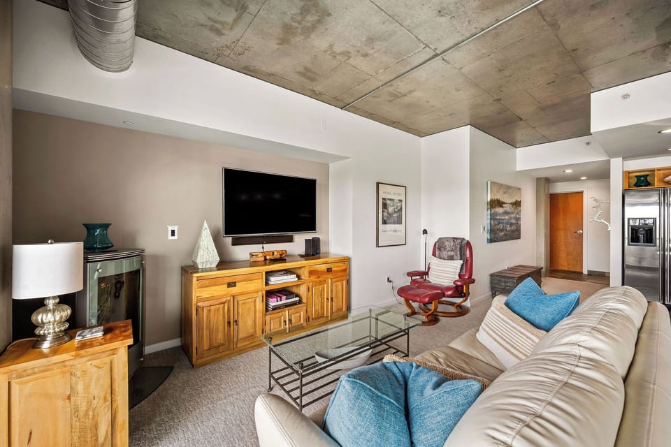 Sink into the plush seating and unwind in your modern living space, where exposed concrete ceilings and warm wood accents create an inviting urban retreat perfect for relaxing after a day of adventure.