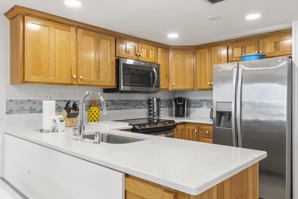 Kitchen features honey-toned wood cabinets, white quartz counters, stainless steel appliances, and a glass tile backsplash.