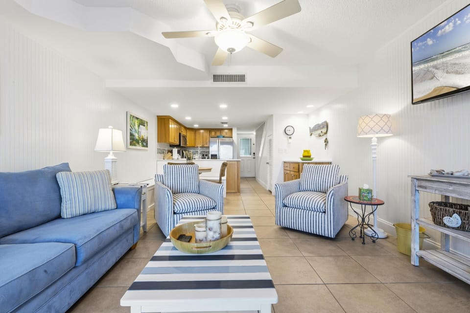 Striped armchairs flank a navy-and-white striped coffee table in the tiled living area under a white ceiling fan.