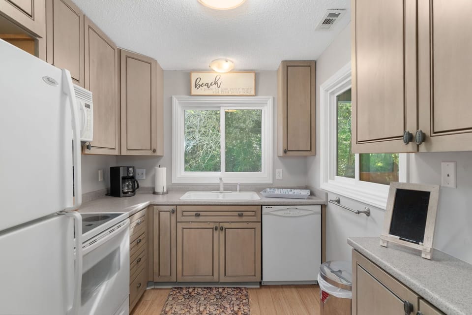 Light and bright kitchen in this Pine Knoll Shores condo, located on the same level as the dining area and overlooking the covered porch. Fully stocked for easy meal prep, this inviting space is perfect for relaxed coastal stays on Bogue Banks.