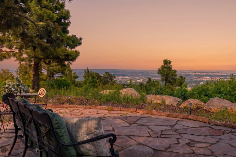 The flagstone patio extends to an open stone seating area at the property's edge, with wrought iron chairs framing an unobstructed panoramic view across the Colorado Springs valley and mountain skyline beyond.
