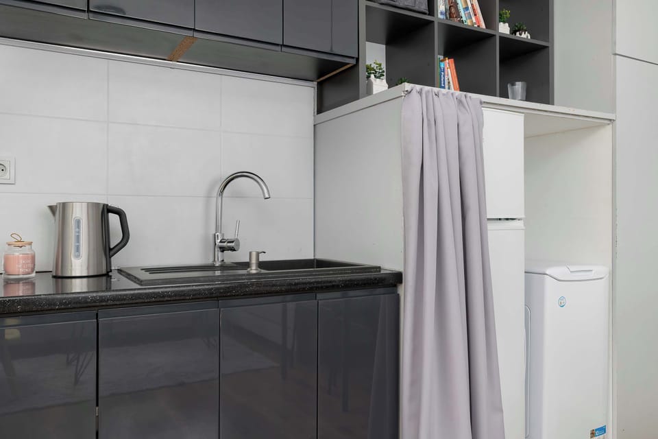 A modern kitchenette with dark cabinets, open shelves, and built-in appliances. The compact space has a clean and stylish design.