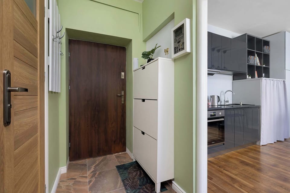 A small entrance area with wooden flooring, wall hooks, and access to the kitchenette. The space looks practical and neatly organized.
