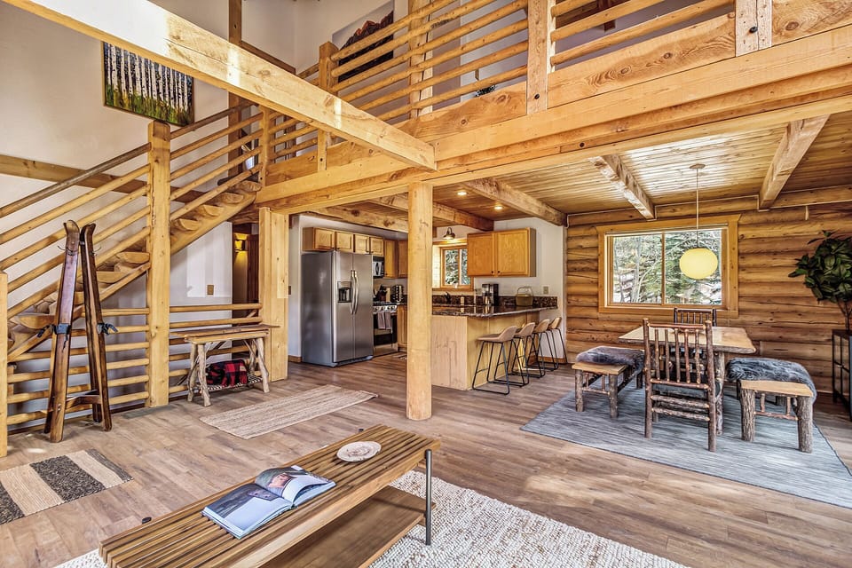 This spacious log cabin great room features soaring ceilings, a cozy stone fireplace, and seamless indoor-outdoor mountain living.