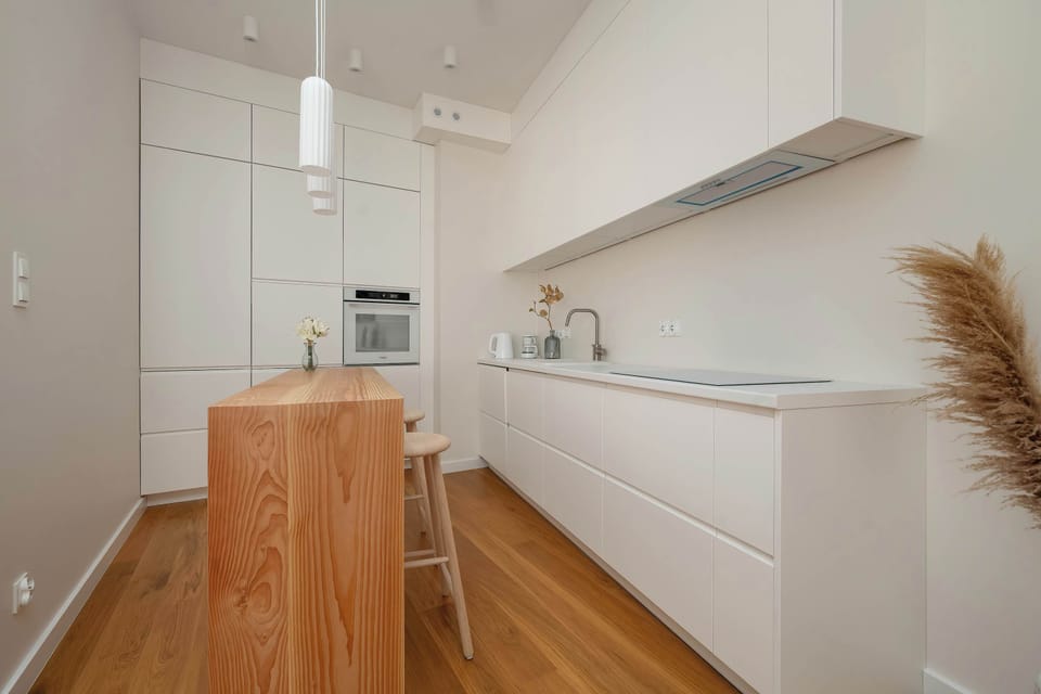 A bright dining and kitchen space with a long counter and modern white cabinetry. Pendant lighting and warm wooden elements enhance the contemporary design.