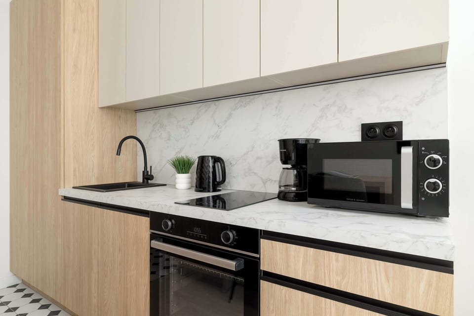 A modern kitchen with light wood cabinets, black countertops, and built-in appliances.