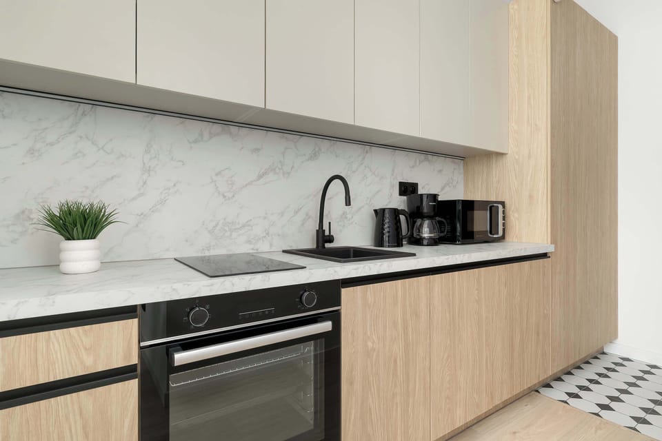 A modern kitchenette with light wood cabinets, marble-style backsplash, and fully equipped appliances.