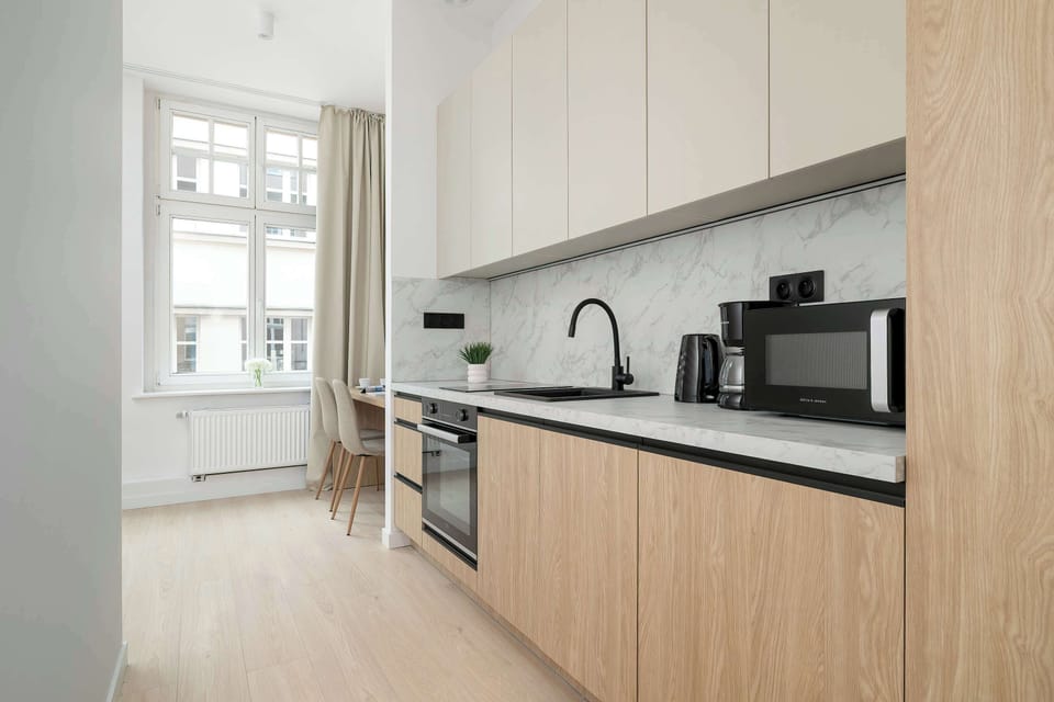 A spacious kitchen area with sleek cabinetry, black countertops, and large windows brightening the space.
