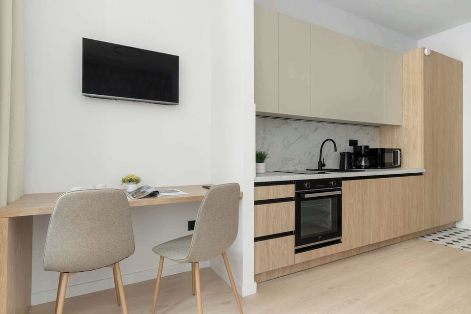 A modern kitchenette with light wood cabinets, marble-style backsplash, and fully equipped appliances.
