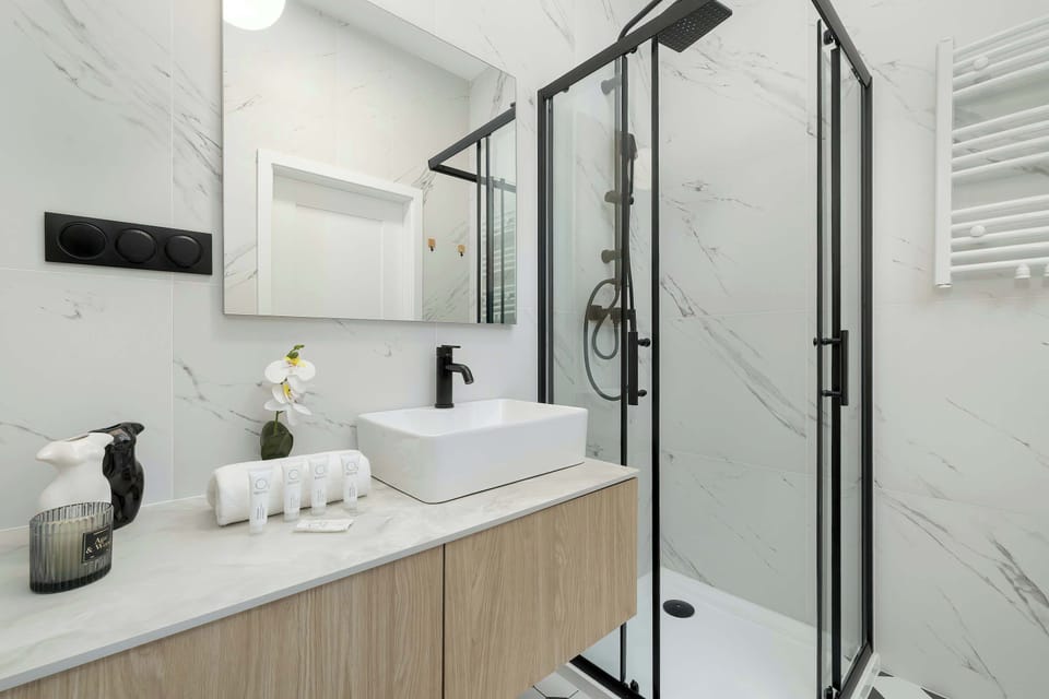 A stylish bathroom with a walk-in shower, modern vanity unit, and elegant black-and-white floor tiles.