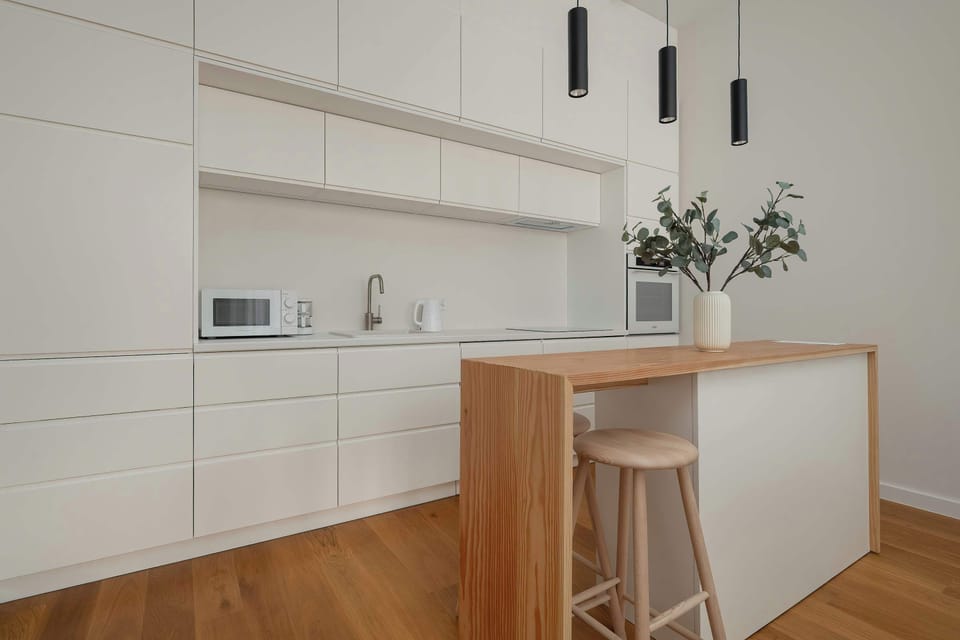 A modern, fully equipped kitchen with sleek white cabinetry and a minimalist design. A wooden island adds warmth and functionality for cooking and dining.