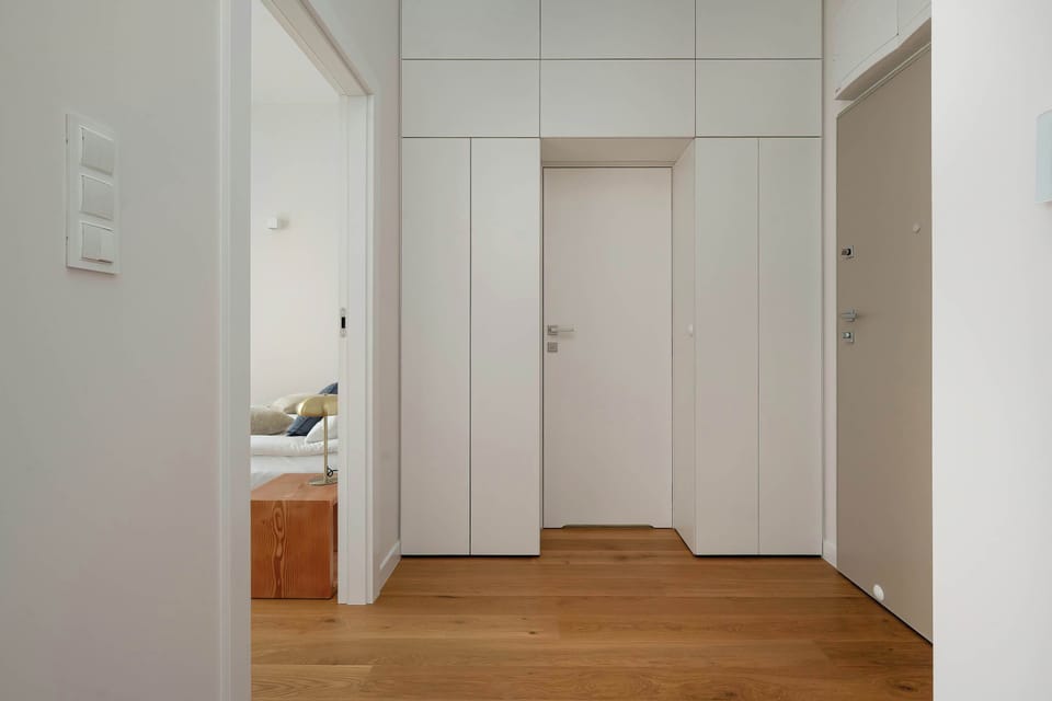 A minimalist hallway with clean white walls and wooden flooring. It provides access to different rooms in a simple, elegant layout.