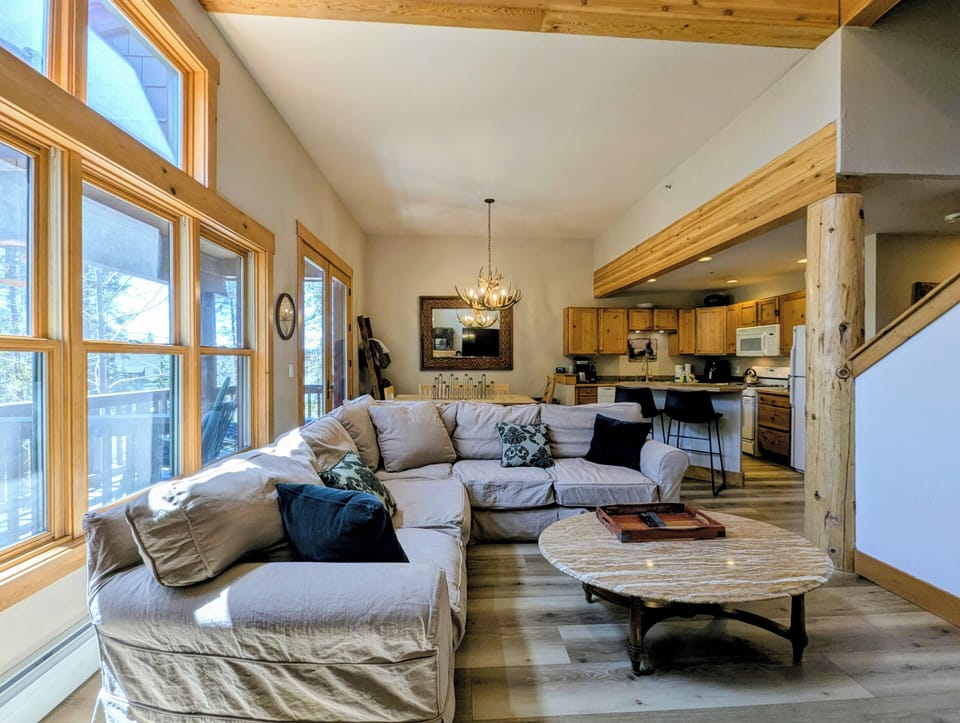 Sunlight pours through floor-to-ceiling windows into this inviting open-concept space where you can unwind on plush seating, enjoy mountain views, and savor the warmth of natural wood throughout.
