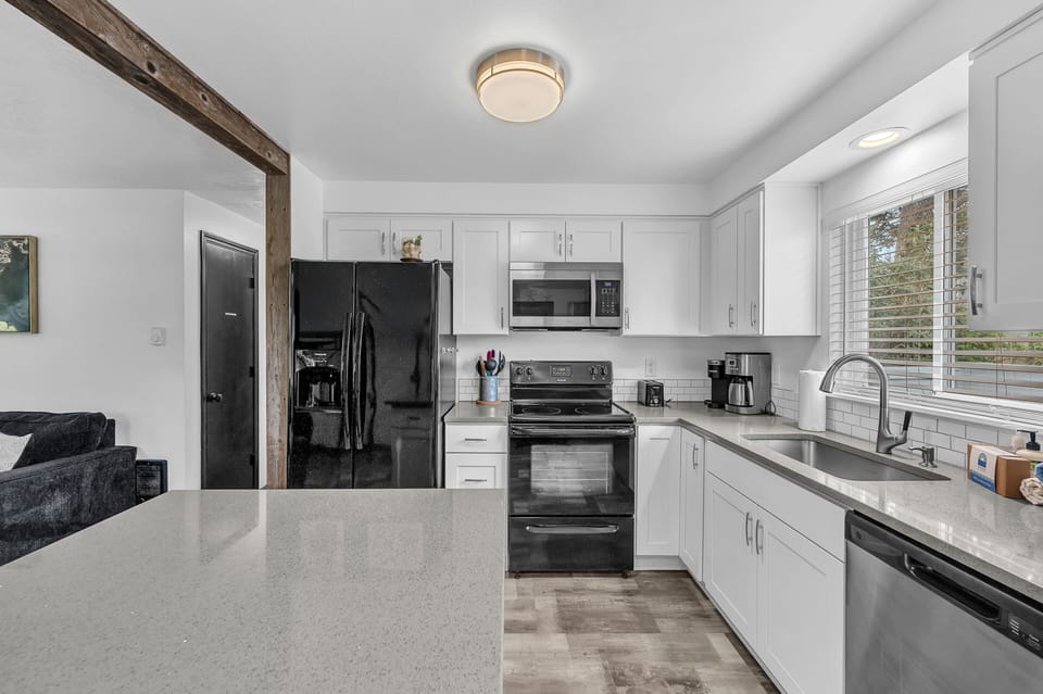Your spacious kitchen features bright white cabinetry, modern appliances, and ample counter space for preparing home-cooked meals, all bathed in natural light from large windows overlooking greenery.