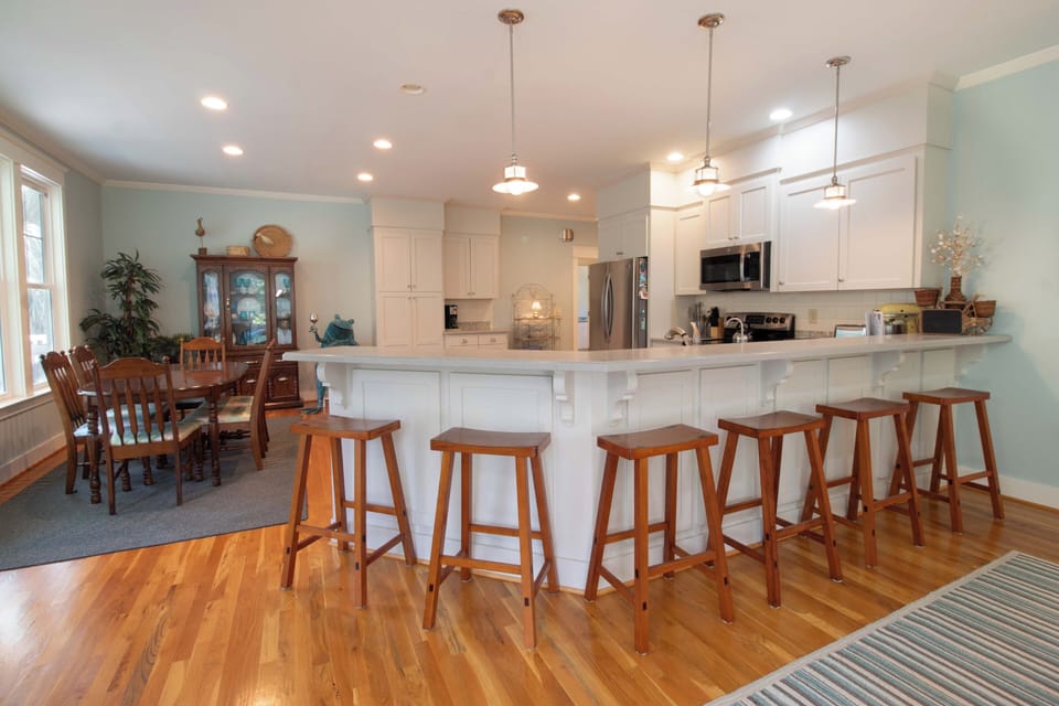 Picture yourself preparing meals in this bright, spacious kitchen with its gleaming white cabinetry, large island seating, and warm hardwood floors—perfect for gathering with your group.