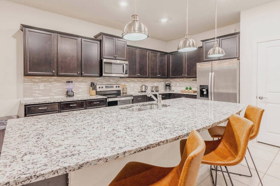 Enjoy the heart of your stay in this stylish kitchen with rich dark cabinetry and a spacious granite island. Modern appliances and warm-toned chairs create a chic atmosphere for cooking and gathering with loved ones.