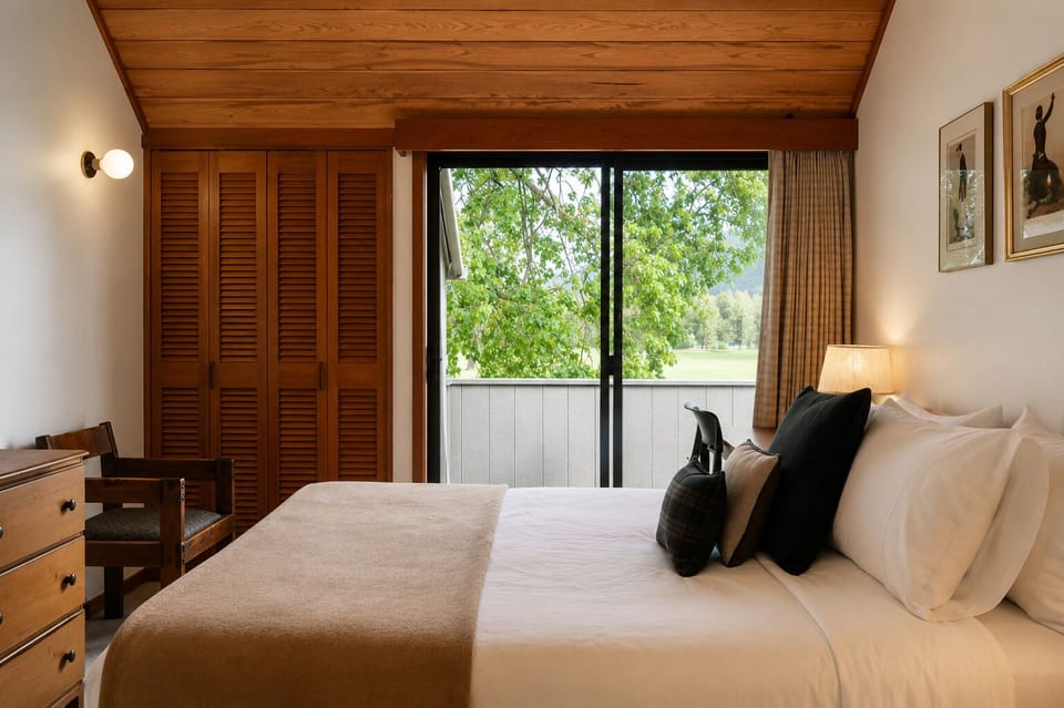 Wake up to lush green views from your cozy bedroom, where warm wooden tones and soft linens invite you to unwind in peaceful comfort.