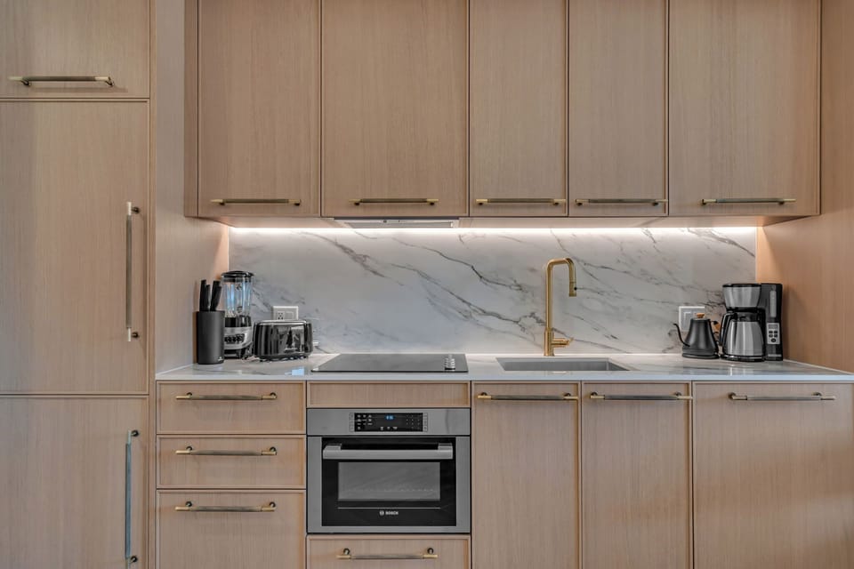Sleek modern kitchen with warm wood cabinetry, quartz countertops, built-in appliances and gold fixtures — beautifully designed for cooking in style