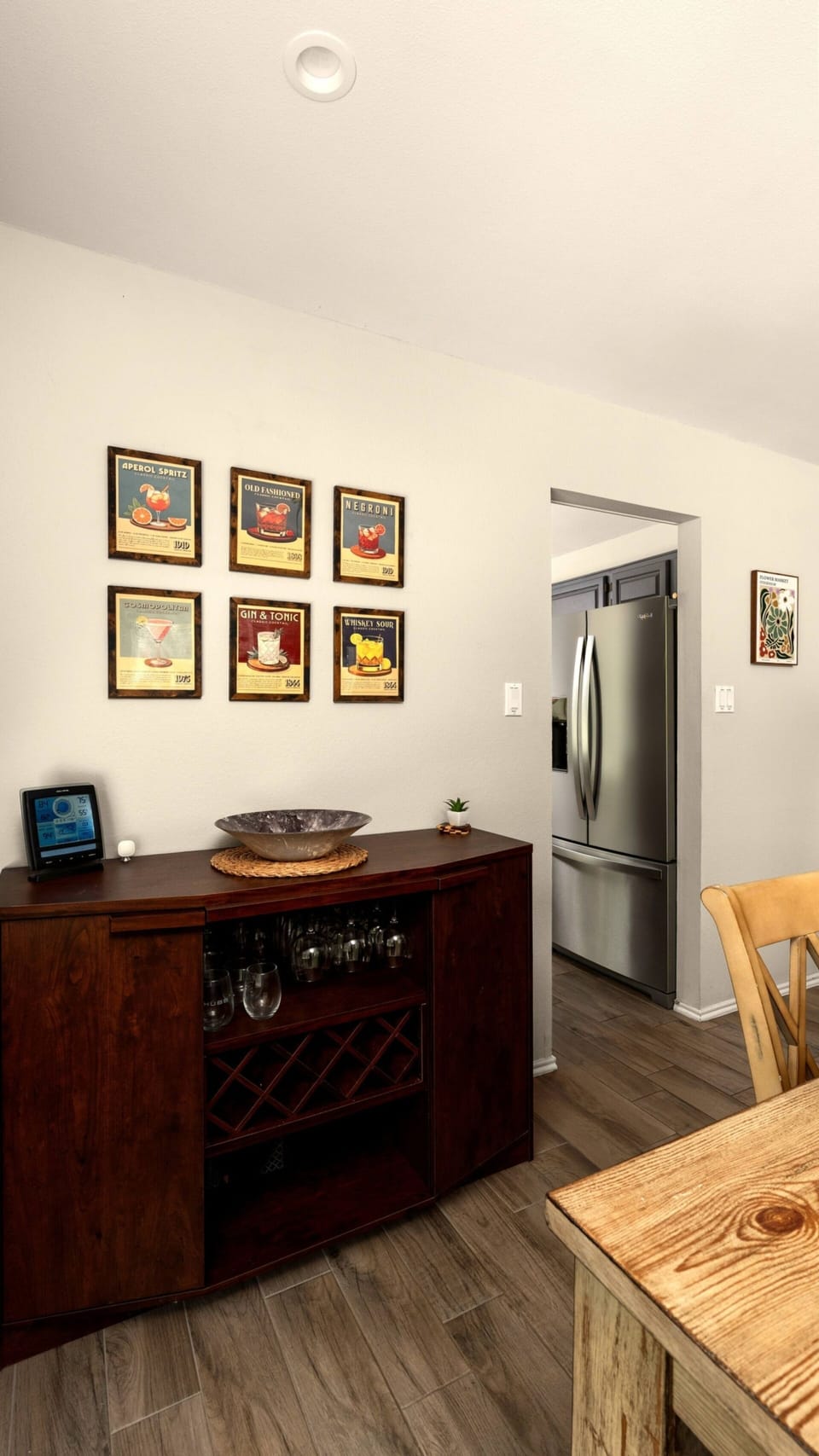 Charming dining vignette with a dark wood wine cabinet, stemware storage, a decorative bowl centerpiece, and a curated gallery of vintage food-and-drink art prints — a warm and personality-filled corner that adds character to every meal.