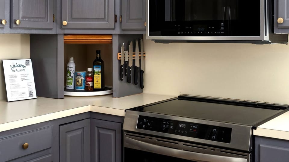 Well-stocked kitchen showcasing grey cabinetry with under-cabinet lighting, a magnetic knife strip, lazy Susan corner organizer, stainless electric range, and microwave — a thoughtfully outfitted cooking space with every detail covered.