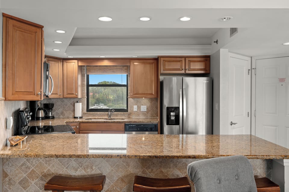 Cook with ease in the full kitchen featuring granite counters, stainless steel appliances, and bar seating.