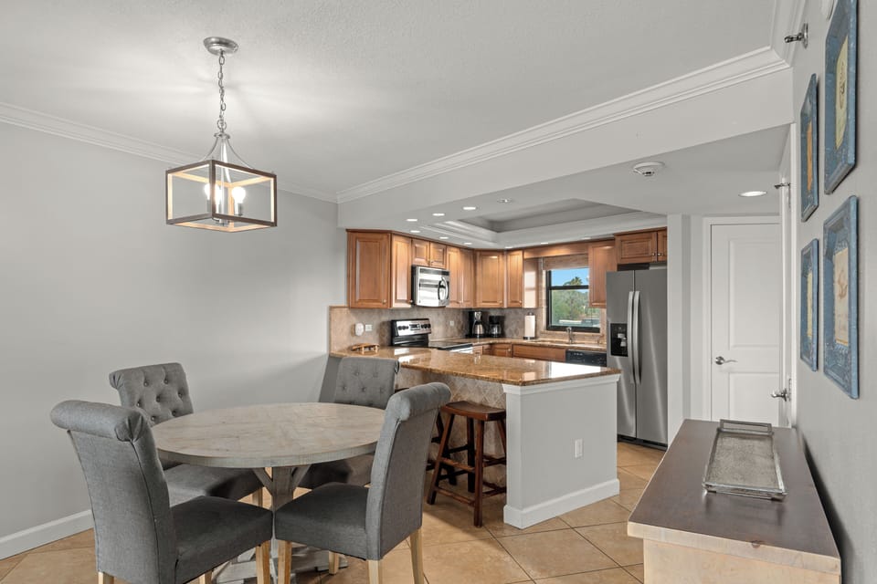 Enjoy meals at the dining table beside a well-equipped kitchen with stainless steel appliances and bar seating.