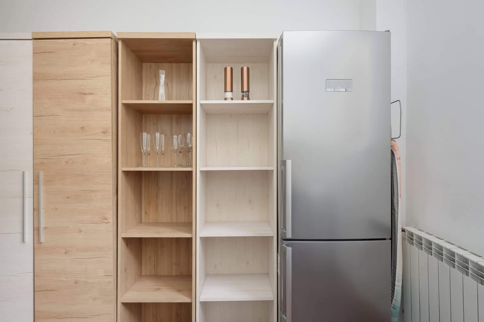 A storage area with open wooden shelving and a stainless-steel refrigerator placed beside it. The organized layout provides practical space for everyday use.