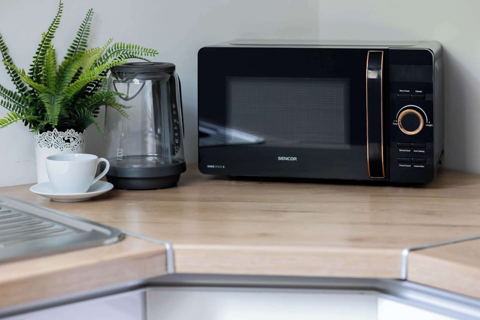 A kitchen countertop with a microwave, coffee machine, and decorative plants arranged neatly in the corner. Clean surfaces and modern appliances add convenience to the interior.
