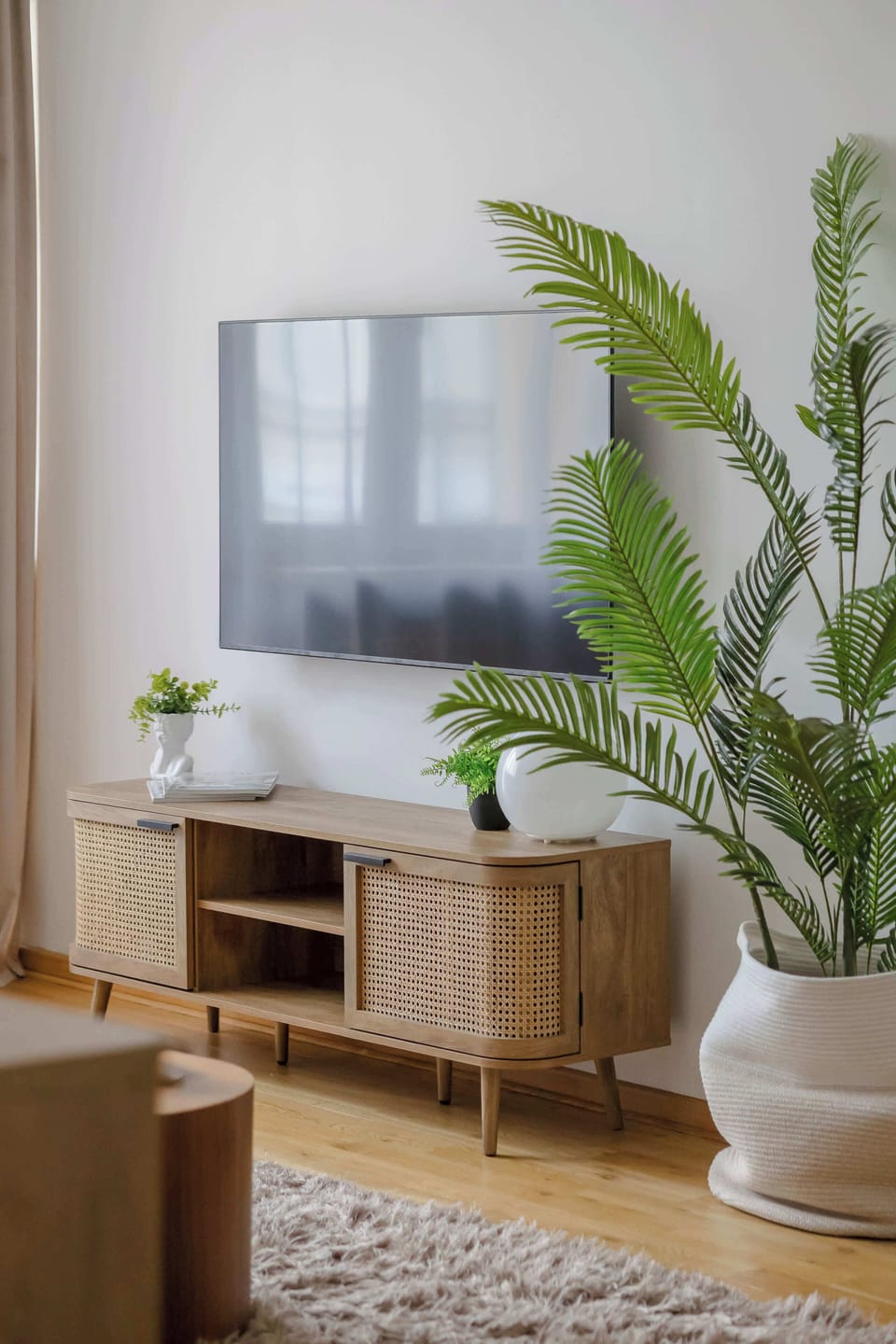 A close-up of the entertainment area with a flat-screen TV, wooden console, and decorative greenery. Minimalist styling gives the room a clean and contemporary appearance.