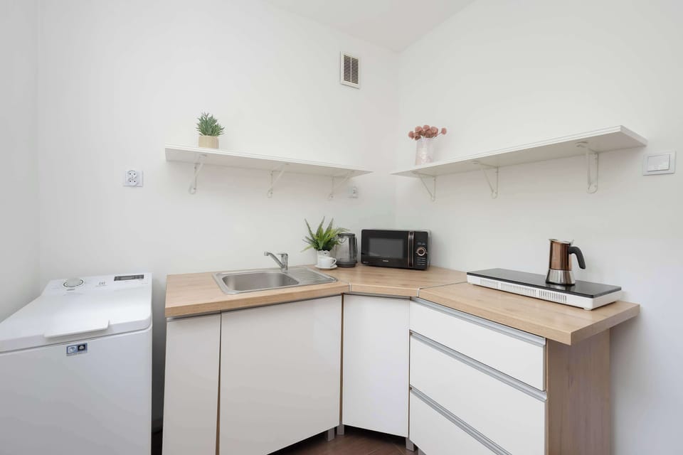 A minimalist kitchen with white cabinets, open shelving, and wooden countertops. Modern appliances and neutral finishes create a sleek cooking area.