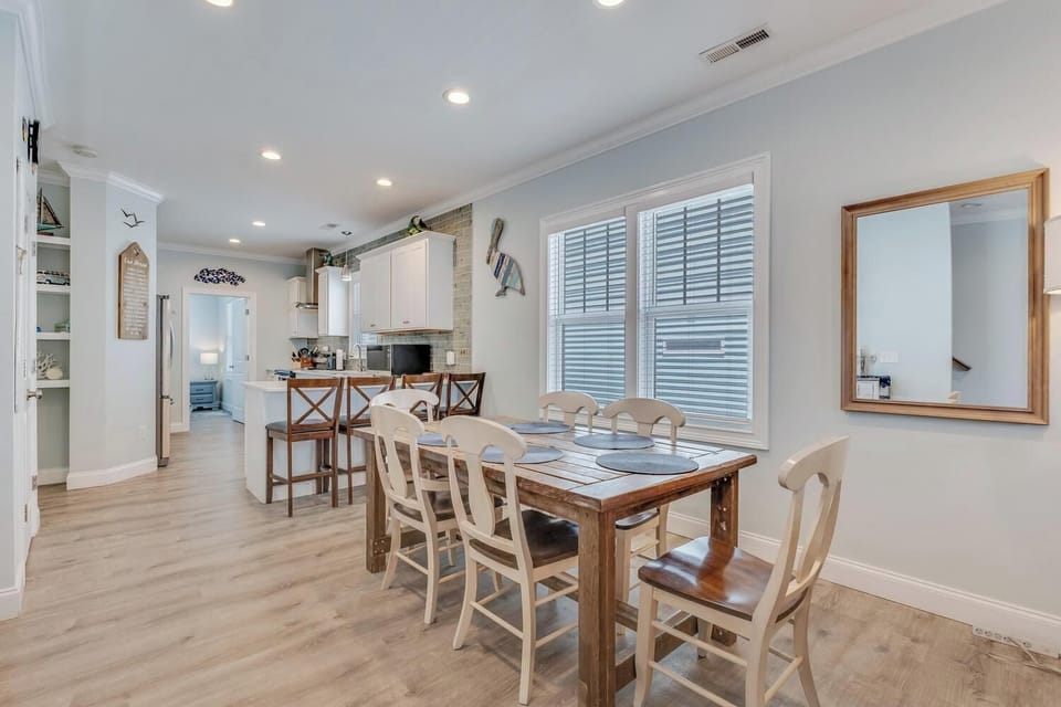 Gather around the rustic dining table for home-cooked meals with loved ones, where natural light streams through plantation shutters, illuminating your coastal-themed haven.