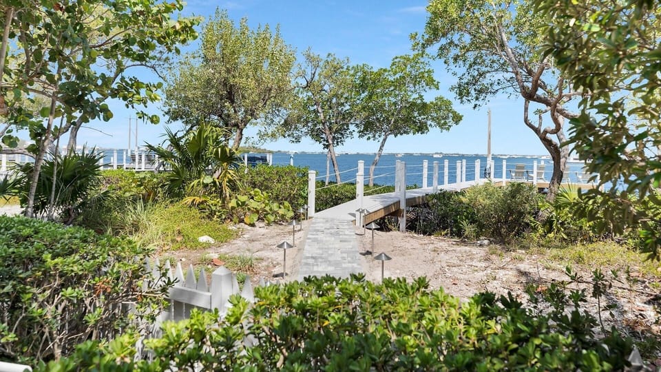 A private walkway winds through coastal greenery toward a serene waterfront dock, offering direct water access and peaceful views of the surrounding bay.
