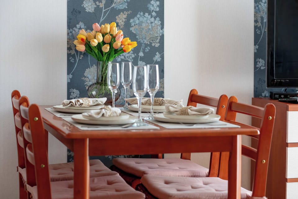 A close-up of a wooden dining table meticulously set with plates, glasses, and a vase of yellow flowers.