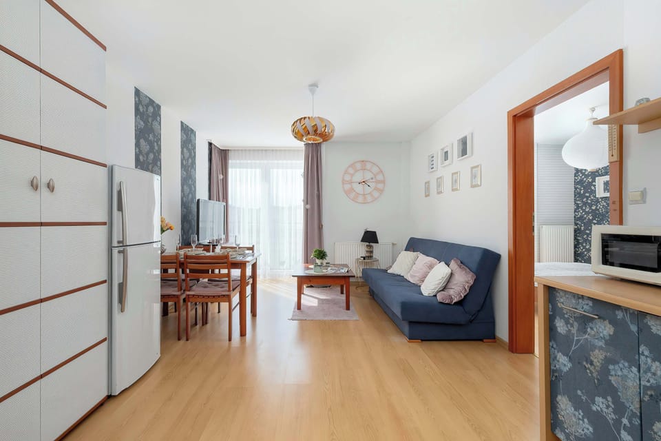 A spacious living room featuring light laminate flooring, a dark blue sofa, and a wooden dining table with chairs.