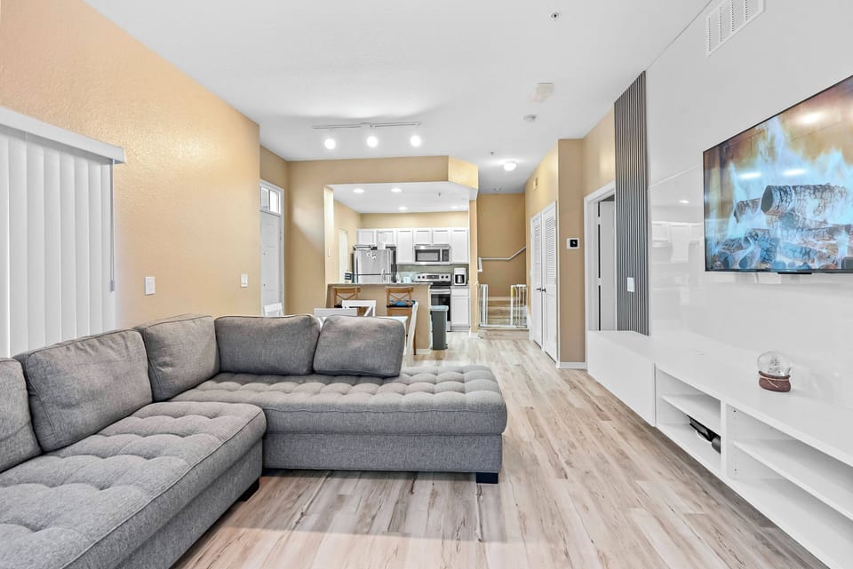 Enjoy a spacious living area featuring a cozy gray sectional ideal for relaxation. Warm golden walls and soft lighting create a soothing atmosphere, complemented by a sleek media console and modern decor for a stylish retreat.