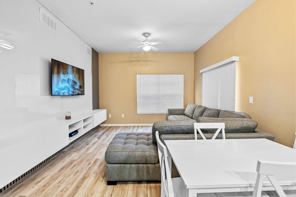 Unwind in the bright living area with a spacious gray sectional sofa, ideal for relaxing after your adventures. Natural light fills the room, enhancing the warm beige walls and stylish decor for a cozy atmosphere.