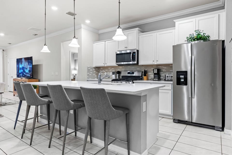 Experience a modern kitchen with sleek gray bar stools and a polished island, ideal for casual dining. The bright white cabinetry and stainless steel appliances create a fresh and inviting space for your culinary adventures.