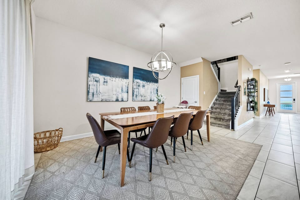 Enjoy meals at the chic wooden dining table under a modern pendant light. The soft beige carpet and elegant art pieces create a warm ambiance, beautifully enhanced by natural light from the large windows.