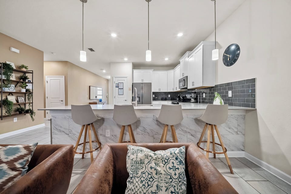 Enjoy our stylish kitchen with sleek white cabinetry, a striking dark backsplash, and light countertops. Cozy bar stools invite casual dining, while the open layout creates a warm, welcoming atmosphere for gatherings.