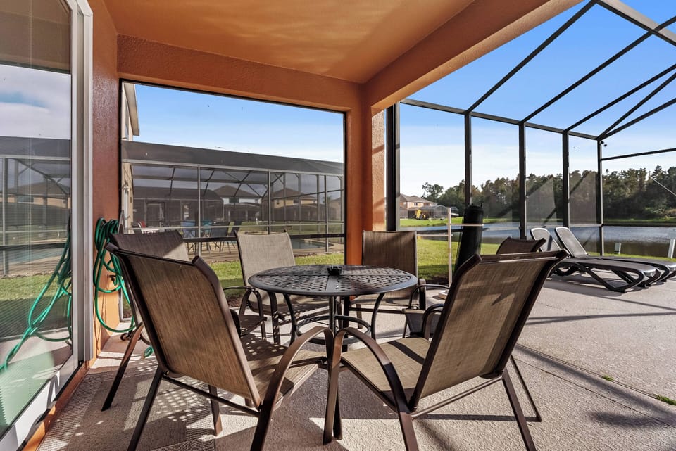 Step onto the screened-in patio, perfect for savoring your coffee at the circular glass table. The warm orange walls and cozy seating blend beautifully with the lush greenery, creating a serene space to relax and unwind.