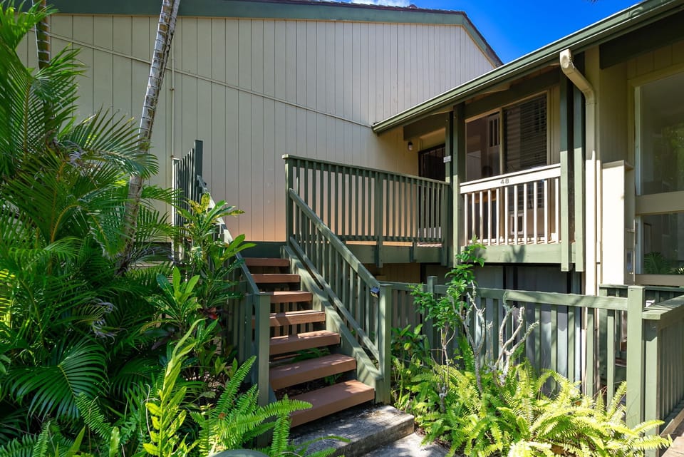 A welcoming property entrance surrounded by lush tropical palms and ferns, creating a serene island atmosphere under bright blue skies.