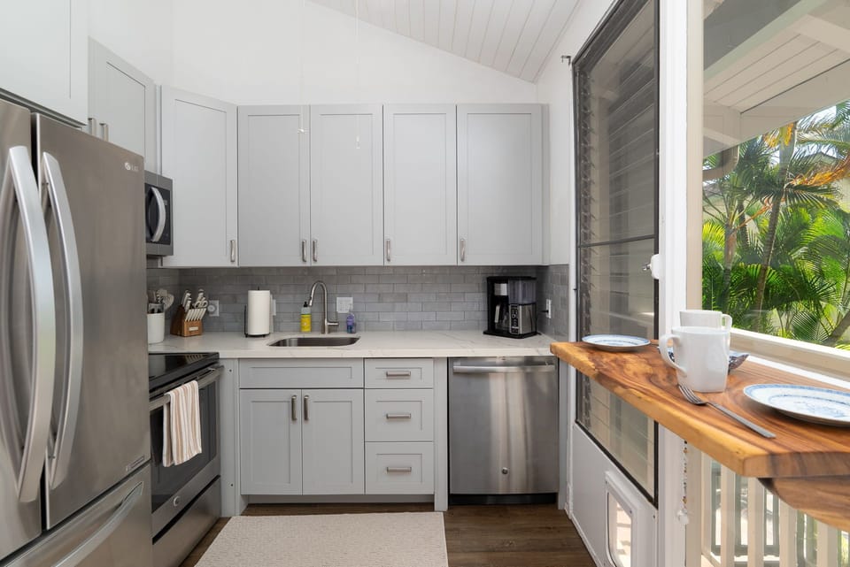 Your bright, modern kitchen features stainless steel appliances and a charming wood breakfast bar where you can sip morning coffee while gazing at lush tropical palms through open windows.