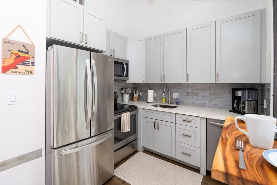 Your fully equipped kitchen features modern stainless appliances, sleek white cabinetry, and stylish subway tile backsplash—ready for preparing meals and morning coffee in comfort.
