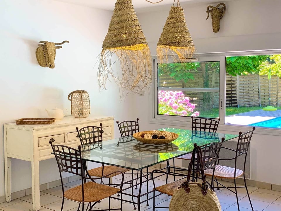 Rattan pendant lights over a glass dining table, with the pool and garden visible through the terrace doors.