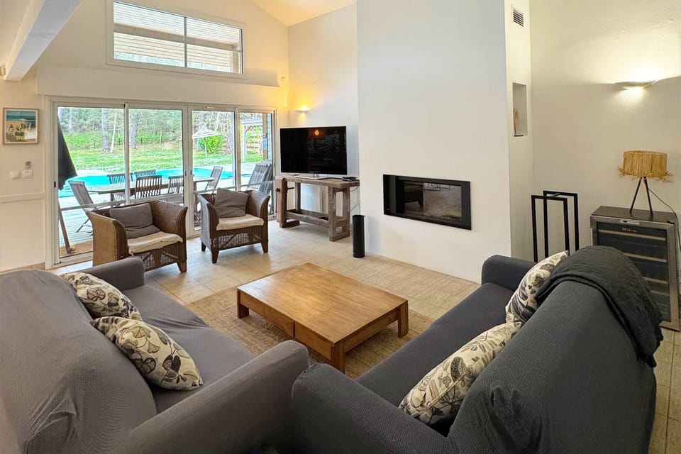 Spacious living room with a fireplace and wooden coffee table — direct access to the garden and pool just beyond the glass doors.