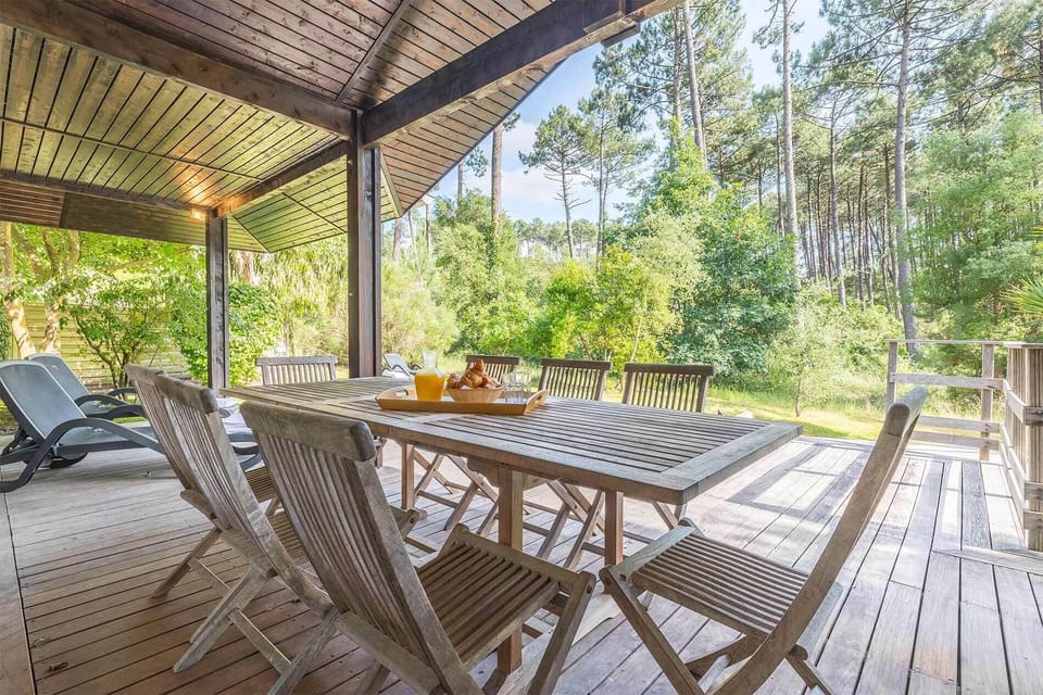 Covered terrace with large wooden dining table, forest views all around, pine trees:<br>Dine al fresco under the covered terrace, surrounded by the sights and sounds of the Landes forest — the perfect setting for long summer evenings.