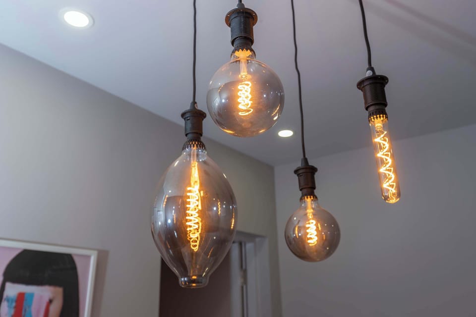 The hanging Edison-style pendant lights add a warm, characterful touch to the space, with their exposed glowing bulbs creating a cosy and inviting atmosphere. The mix of shapes and suspended heights gives the decor a modern yet distinctive feel.
