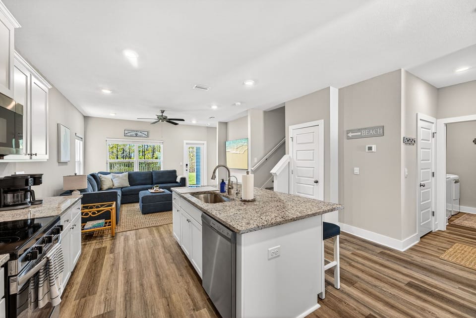 Step into an open, airy space where the kitchen flows seamlessly into the living area. Natural light fills the room, highlighting granite countertops, modern appliances, and a cozy spot to unwind after your beach adventures.