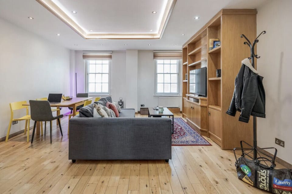 Full living room showing both period windows, Smart TV, oak unit and air conditioning — a genuinely generous space moments from Oxford Street.