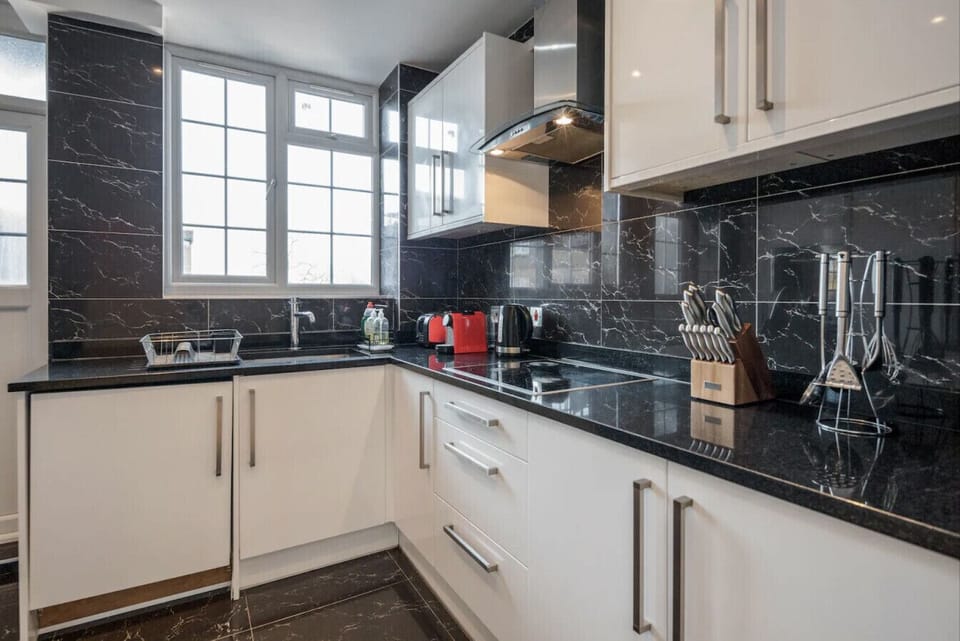 Well-equipped kitchen with induction hob, Nespresso machine, kettle and full storage — natural light and black marble finish throughout.
